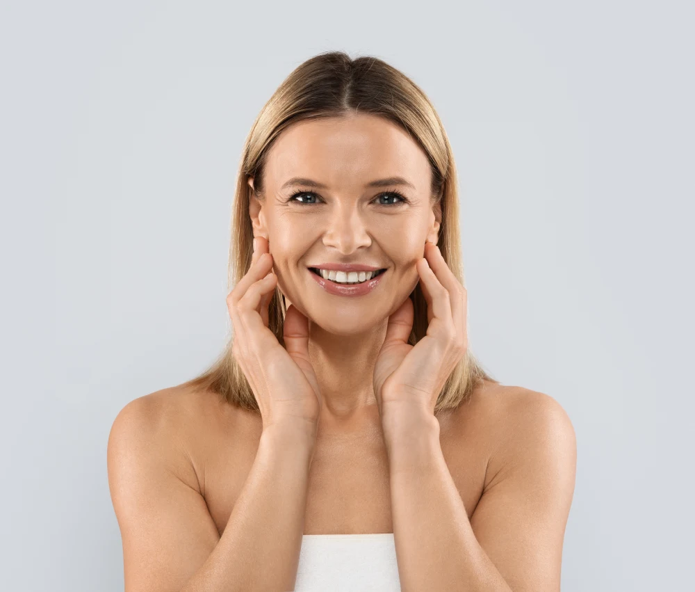 Smiling blonde woman framing her face with both hands to display supple, plump skin volume
