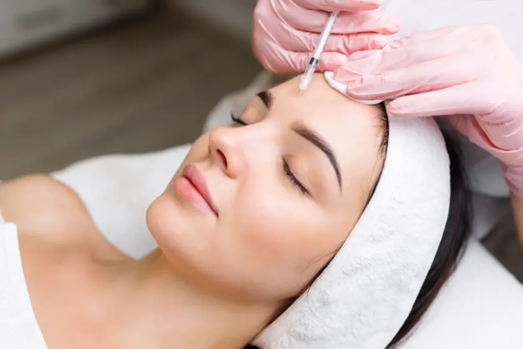 Client wearing a pink spa headband receiving a Botox injection on the forehead