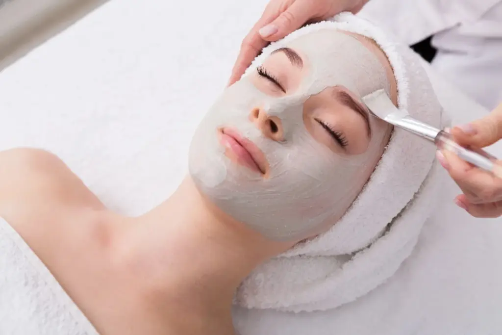Client wearing a spa headband receiving a purifying white clay or cream facial mask