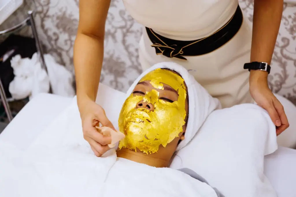 Client resting on a spa table wearing a luxurious gold mask treatment