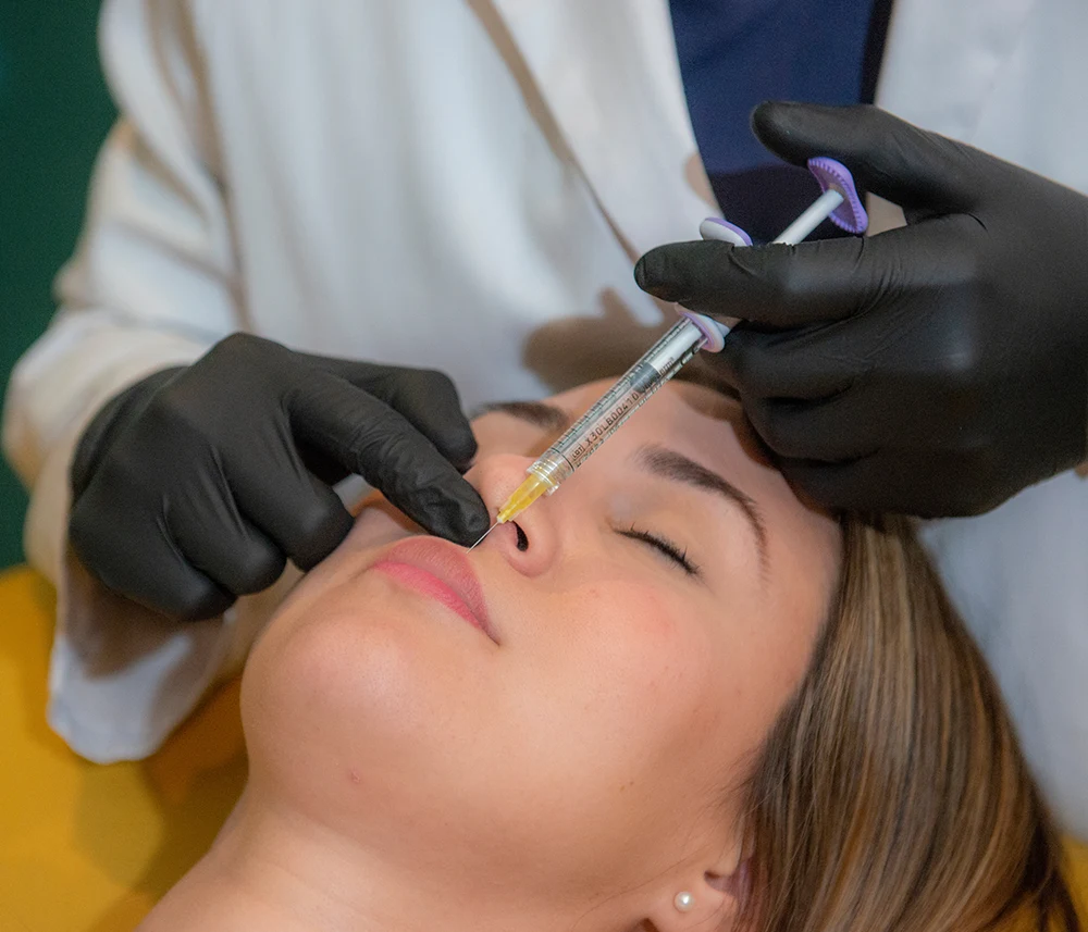 Practitioner wearing black medical gloves administering a Radiesse filler injection
