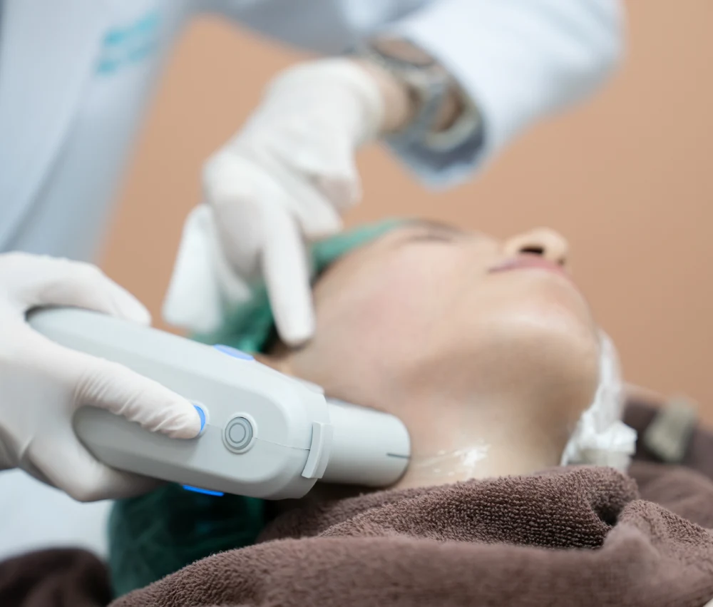 Aesthetician in white gloves using an Ultherapy device on a client's face.