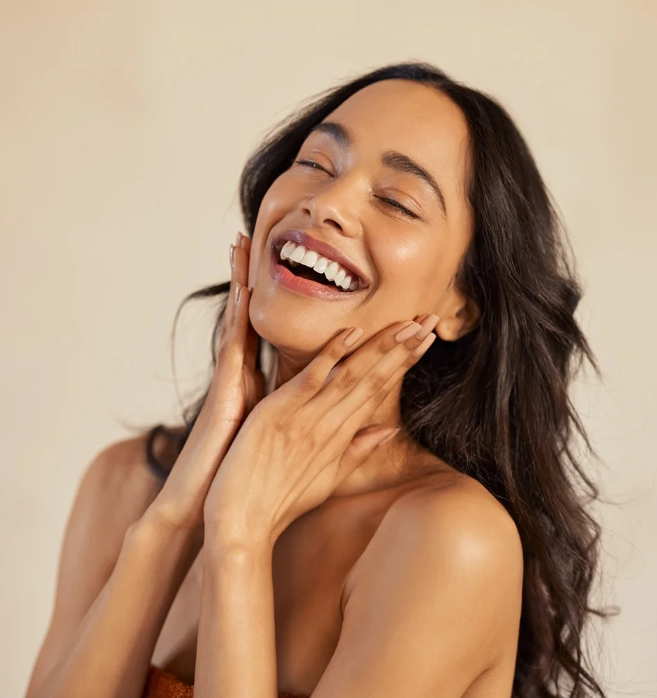 Woman with dark curly hair laughing joyfully, showcasing smooth skin after mole removal