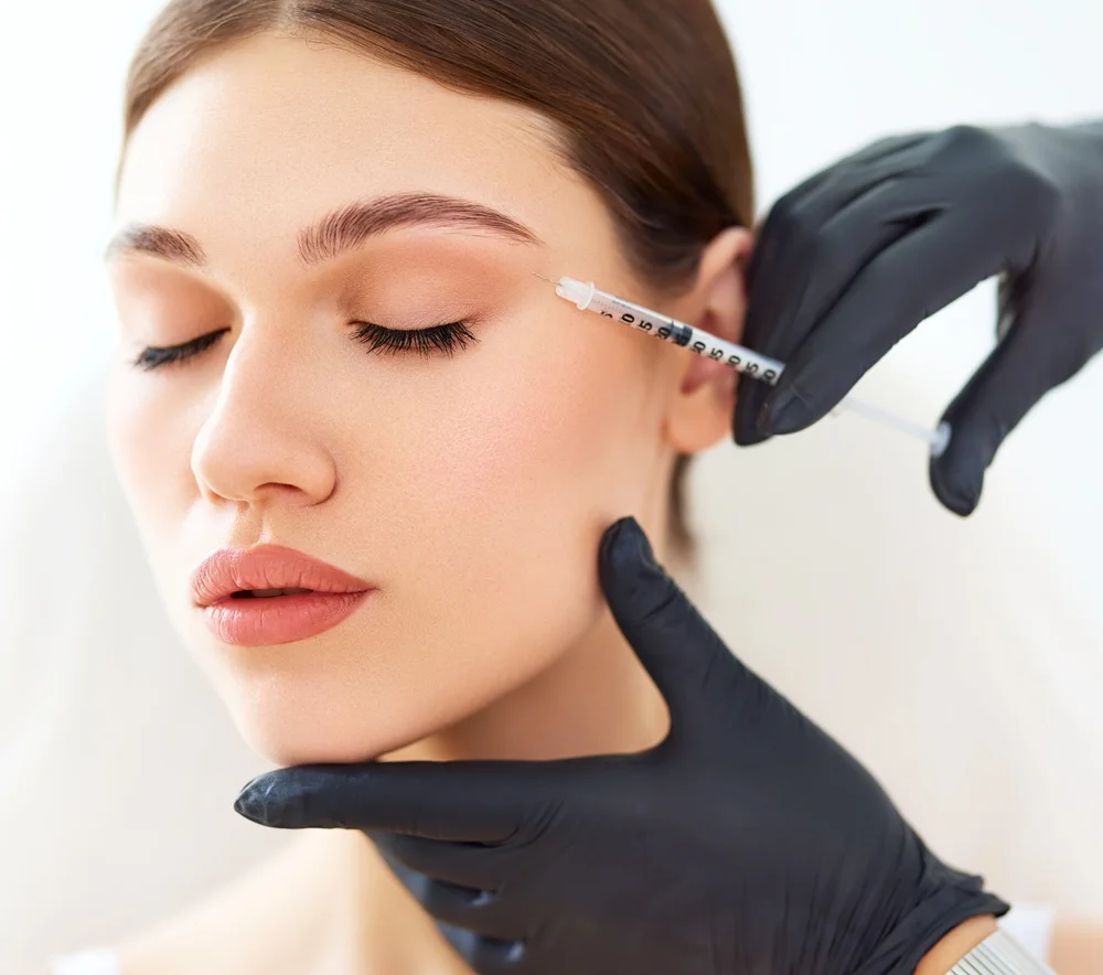 Client receiving Xeomin neurotoxin injection between eyebrows from a gloved provider.